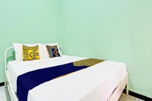 Una cama blanca con almohadas amarillas y azules. en SPOT ON 92012 Homestay Grand Mahkota Permai Syariah, en Cilacap