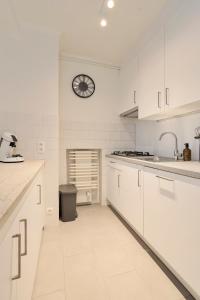 a kitchen with white cabinets and a clock on the wall at Flat Henri in De Panne +8 photos