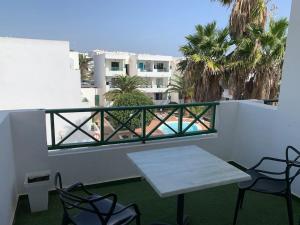 een witte tafel en stoelen op een balkon met palmbomen bij Coqueto apartamento ZUA con piscina in Costa Teguise