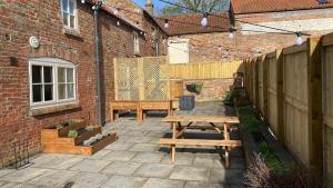 a patio with two picnic tables and a brick building at The Stables - Quirky one bed holiday home with wood fired hot tub in Rudston