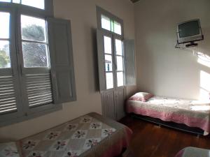 a room with two beds and a tv and windows at Pousada Gameleira in Diamantina