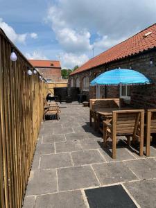 a patio with benches and a blue umbrella at The Shires - Quirky 3 bed holiday home with Wood-fired Hot-tub in Rudston