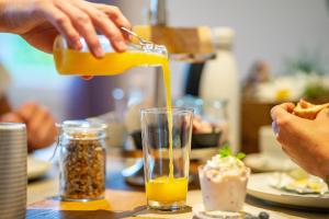 osoba wylewająca sok pomarańczowy do szklanki na stole w obiekcie Gästehaus Aemisegg w mieście Sankt Peterzell