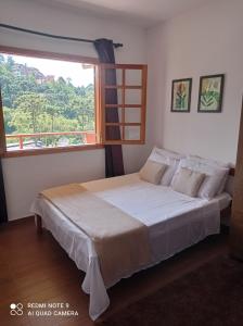 a bedroom with a bed with a large window at Cantinho Feliz a 900m do Capivari in Campos do Jordão