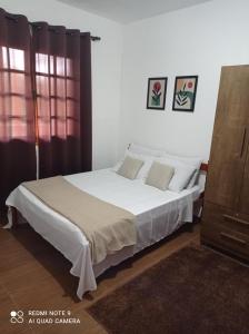 a bedroom with a bed with white sheets and pillows at Cantinho Feliz a 900m do Capivari in Campos do Jordão