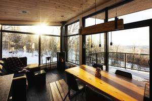 uma sala de estar com uma mesa de madeira e janelas grandes em Le Zéphyr - Domaine Maelstrom em Lac-Beauport