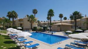 una piscina con sillas, sombrillas y palmeras en Jardins Vale de Parra, en Albufeira