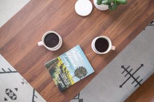 two cups of coffee and a book on a table at Downtown Picton 2-Bedroom Boho Suite! in Picton