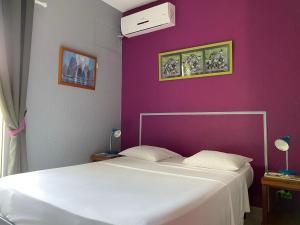 ein Schlafzimmer mit einem weißen Bett und einer lila Wand in der Unterkunft Hotel La Chaumiere in Matoury