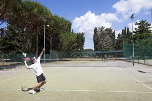 a man serving a tennis ball on a tennis court at Camping Village Oasi in Albinia