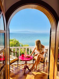 a woman sitting at a table on a balcony overlooking the ocean at Byblos Mare in Skala Sotiros