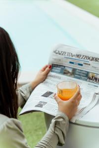 a woman reading a newspaper with a glass of juice at Tuo Hotel in Polignano a Mare