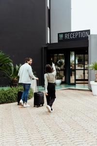 two people walking in front of a building with luggage at Tuo Hotel in Polignano a Mare
