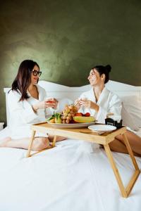 two women sitting on a bed with a table with a plate of food at Tuo Hotel in Polignano a Mare