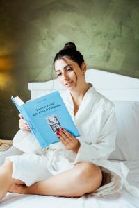 a woman sitting on a bed reading a book at Tuo Hotel in Polignano a Mare