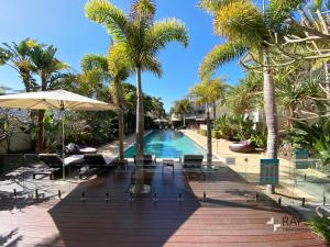 a pool with palm trees and chairs and an umbrella at Bali Luxury Resort - Holiday Management in Kingscliff
