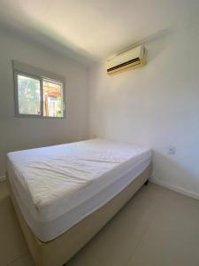 Dormitorio blanco con cama y ventana en Casa tranquila 500 metros da praia do campeche en Florianópolis