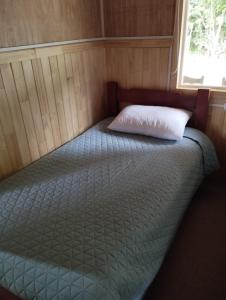 Bett in einem Zimmer mit Kissen und Fenster in der Unterkunft Cabañita Sustentable El Este Cochamó in Cochamó