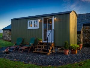 a green tiny house with chairs and a patio at The Pleasant Hut at MountPleasant Farm in Ulverston