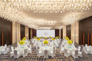 un salón de banquetes con mesas y sillas blancas y lámparas de araña en Crowne Plaza Zhengzhou High Tech Zone, an IHG Hotel, en Zhengzhou
