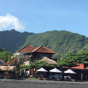 a building with tables and umbrellas in front of a mountain at Amed Sunset Beach in Amed