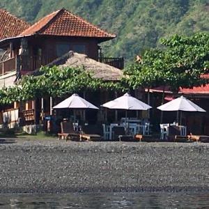 a building with tables and umbrellas next to the water at Amed Sunset Beach in Amed