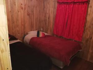 リナレスにあるCabaña en linares camino el embalse ancoaのベッド2台と赤いカーテンが備わる小さな客室です。