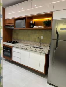 cocina con armarios blancos y nevera de acero inoxidable en Apartamento Concierge Sensacional, en Marabá