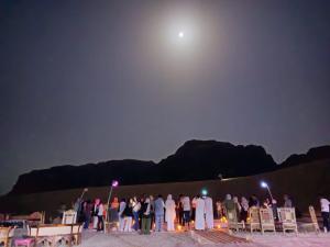 a group of people standing around under a full moon at Mozoon camp in Wadi Rum