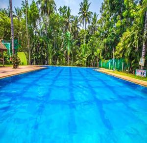 a large blue swimming pool with trees in the background at FabEscape Queens Paradise in Puducherry