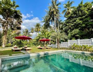 a swimming pool with two red umbrellas and two chairs at Parasol Blanc in Luang Prabang