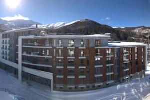 a large brick building with mountains in the background at Cozy Apartment in Orbi Bakuriani in Bakuriani