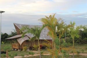 Hanchey Bamboo Resort في كامبونغ تشام: منزل صغير بسقف من القش بجوار أشجار النخيل