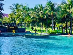 a swimming pool with palm trees in a resort at Sonata Resort & Spa in Phan Thiet