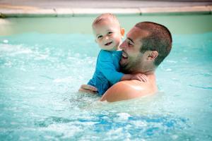 a man holding a baby on his back in a swimming pool at Camping Park Er Lann in Saint-Pierre-Quiberon