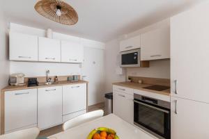 una cocina con armarios blancos y un bol de fruta en una mesa en La Perle du Port * Terrasse * clim * mer à 5 min * chambre *, en Carnon-Plage