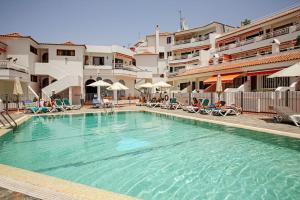 una piscina en un hotel con sillas y sombrillas en Royal Suite Diamantes I With heated pool en Los Cristianos