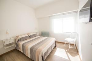 een witte slaapkamer met een bed en een stoel bij Corrientes Suites in Mar del Plata