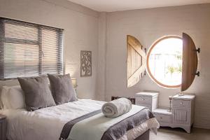 a white bedroom with a bed and a window at Dragon Tree in Yzerfontein