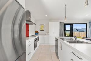 La cuisine est équipée de placards blancs et d'un réfrigérateur en acier inoxydable. dans l'établissement Puna Rise - Taupo Holiday Home, à Taupo