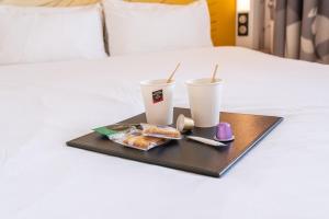 a tray with two cups and food on a bed at B&B HOTEL Bordeaux Bassins à flot in Bordeaux