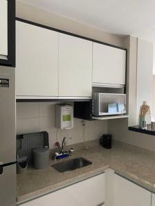 cocina con armarios blancos, fregadero y microondas en LINDO LOFT, PISCINA, ESTACIONAMENTO, ACADEMIA, AR CONDICIONADO, Wi-Fi, en São Paulo