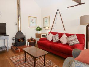The Bull Pen في Colyton: غرفة معيشة مع أريكة حمراء وموقد خشب