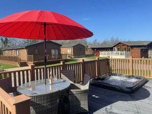 - une table avec un parasol rouge et une baignoire sur la terrasse dans l'établissement Little Gem Lodge with Hot Tub, à Malton