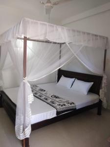 a bedroom with a canopy bed with white sheets and pillows at Prasai House in Ahangama