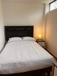 een slaapkamer met een groot wit bed en een lamp bij Apartamento familiar a 10 min auto de Plaza Armas Lima in Lima