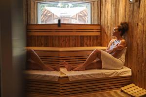 a woman sitting on a bed in a sauna at Hotel Olangerhof in Valdaora