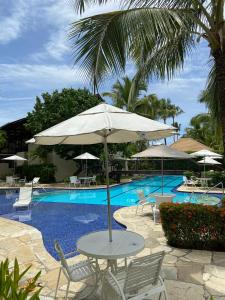a table with an umbrella next to a swimming pool at Nannai Residence Porto Galinhas Praia Muro Alto 101 in Porto De Galinhas