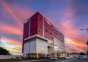 un edificio alto de color rojo con una puesta de sol en el fondo en Ramada Encore by Wyndham Guadalajara Aeropuerto, en Guadalajara