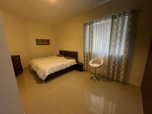 1 dormitorio con 1 cama y ventana con silla en The Village Apartment 2, en Kirkop